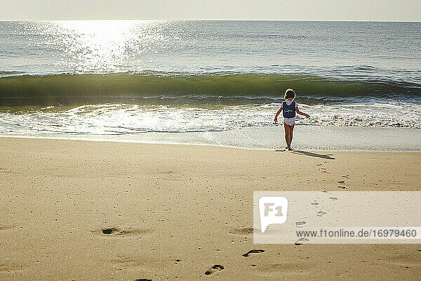 A little girl walks across golden sand on beach to the ocean