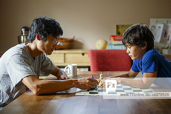 A father and son sit together at a table playing a game of chess