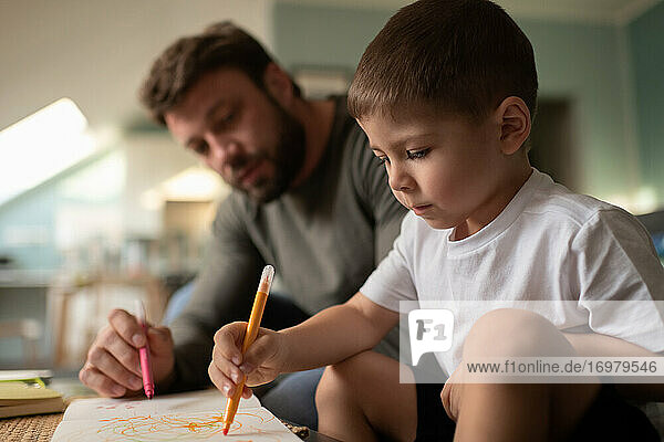 Konzentrierter Junge  der mit seinem Vater zeichnet