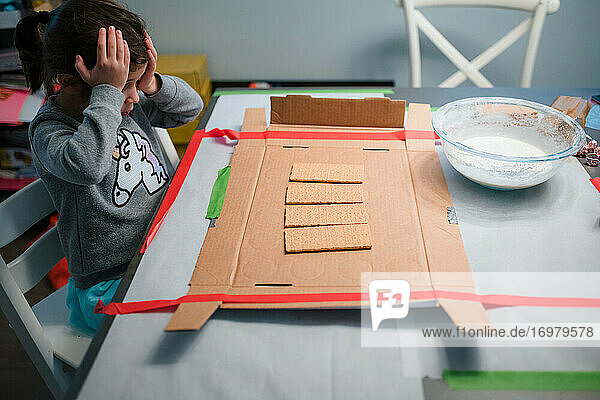 Mädchen Lebkuchenhaus Projekt Hände auf dem Kopf am Tisch