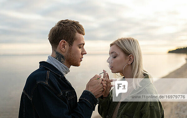 Junger Mann und Frau rauchen am See
