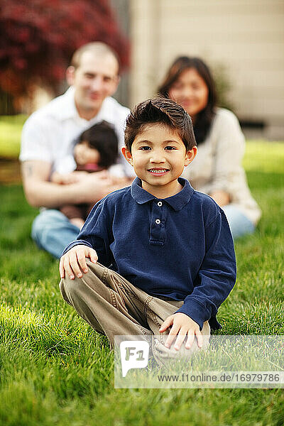 Junge sitzend und lächelnd vor seiner Familie im Gras
