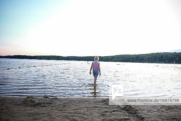 Mädchen geht ins Wasser am See bei Sonnenuntergang