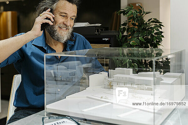 Älterer Mann mit Bart telefoniert und betrachtet ein Gebäudemodell. Architektur Konzept