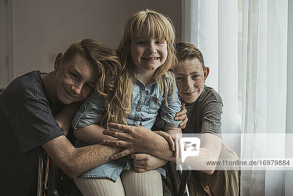 Portrait of brothers hugging beautiful little sister in wheelchair