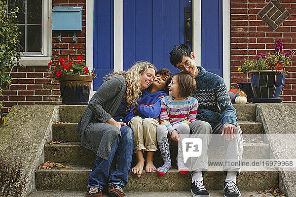 A loving family snuggle together on front stoop of home in autumn