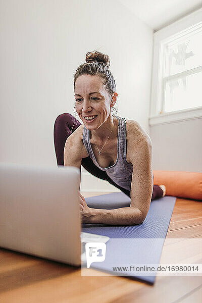 Woman smiles while using computer to practice yoga in her home