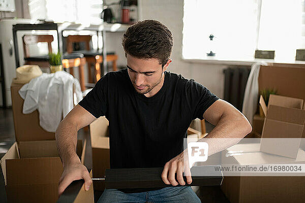 Junger Mann beim Zusammenbau eines Tisches in seiner neuen Wohnung