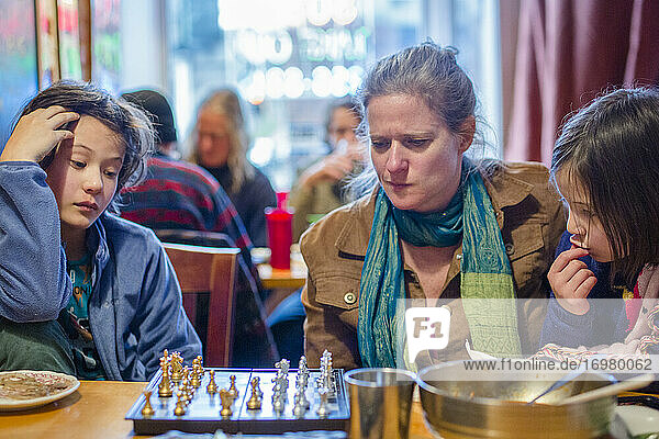 Eine Frau und Kinder sitzen zusammen in einem Restaurant und studieren ein Schachbrett