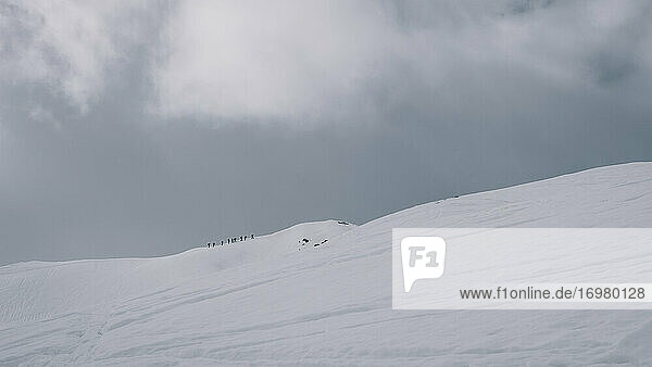Alpinisten beim Versuch  einen schneebedeckten Berggipfel an einem bewölkten Tag zu besteigen