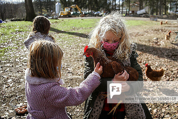 girl with blonde hair holding chicken on a farm