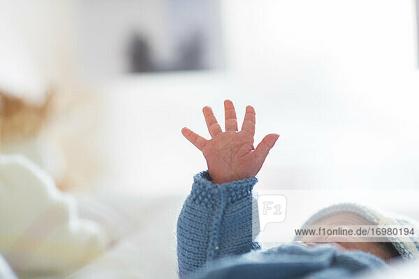 ein Neugeborenes in seiner Wiege hebt seine Hand
