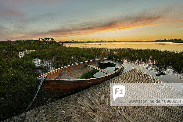 Verlassenes Boot und Steg in der Nähe der grasbewachsenen Küste bei Sonnenuntergang