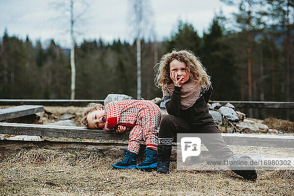 Junge und Mädchen sitzen auf einem Holzstamm und langweilen sich im Winter im Wald