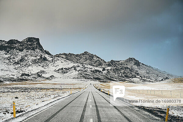 Verschneite Straße und Berge an einem bedeckten Tag