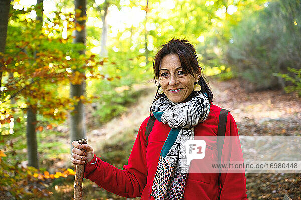 Lächelnde Wanderin  die einen Stock in den Wald hält und in die Kamera schaut