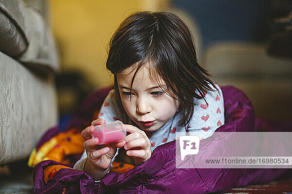 Ein kleines Mädchen liegt in einem Schlafsack auf dem Boden und studiert eine Tube mit Flüssigkeit