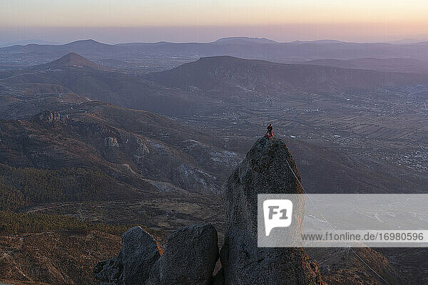 One man standing at the top of a high exposed rock setting a slickline