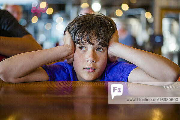 Ein Junge mit dem Kopf in den Händen sitzt am Restauranttisch und wartet geduldig