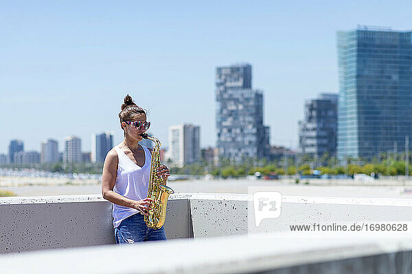 Woman with ponytail playing a saxophone while standing outdoors