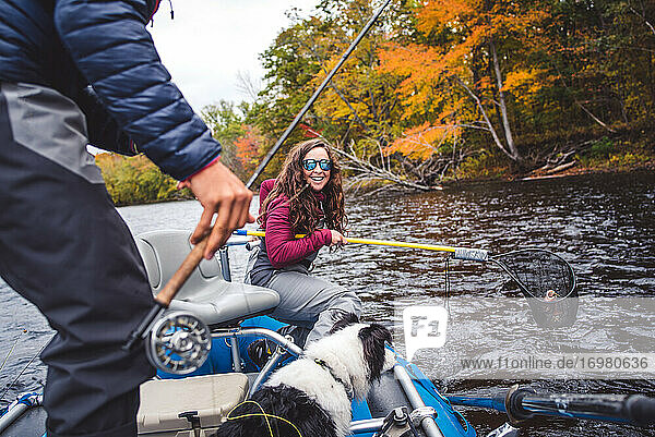 Frau in Wathose lächelt  nachdem sie einen Fisch im Herbstlaub gefangen hat
