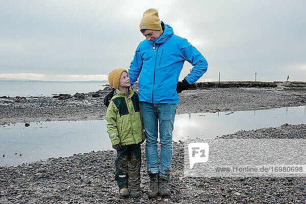 father and son stood together at the beach covered in mud smiling