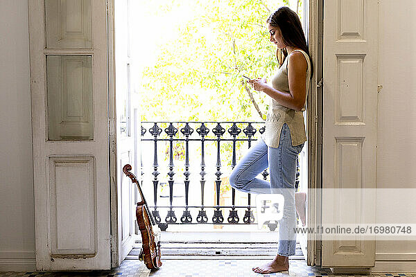 Ein barfuß gehendes Mädchen vor einem sonnigen Balkon mit einem Mobiltelefon.