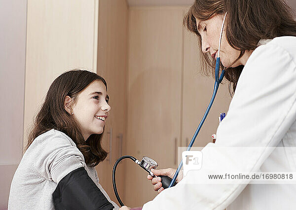 Ärztin  die den Druck auf den Arm eines Mädchens in ihrem Bett untersucht. Hausarzt-Konzept