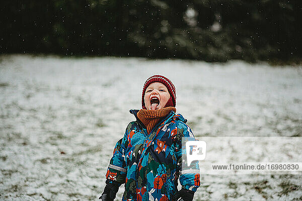 Niedliches Kind streckt seine Zunge heraus und probiert Schneeflocken im Winter