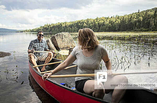 Afrikanischer Mann und weiße Frau in rotem Kanu auf einem See in den Wäldern von Maine.
