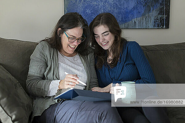 A mother and daughter laugh while looking at a tablet together