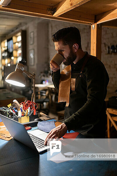 Handwerker  der ein Heißgetränk trinkt und einen Laptop benutzt