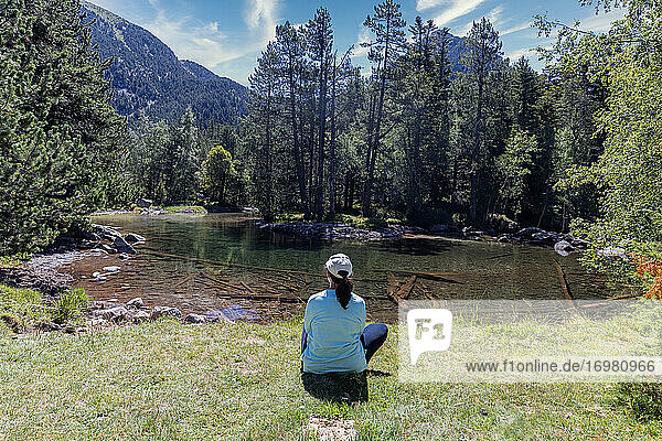 Middle aged woman sitting by transparent mountain lake and looking forward to landscape  Mountain Pyrenees