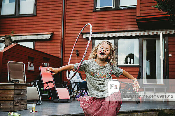 Cute girl having fun with hula hoop in backyard with red wooden house