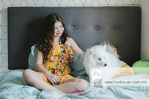 Junges Mädchen sitzt auf einem Bett und streichelt einen süßen kleinen flauschigen weißen Hund