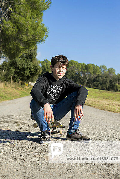 Gutaussehender Teenager mit einem Skateboard auf einer asphaltierten Straße sitzend