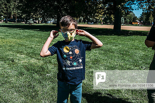 Young boy adjusting face mask outside at park on sunny day