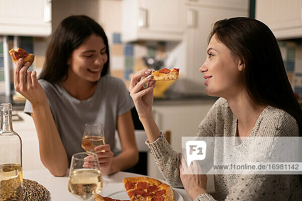 Glückliche junge Frauen mit Pizza im Gespräch in der Küche