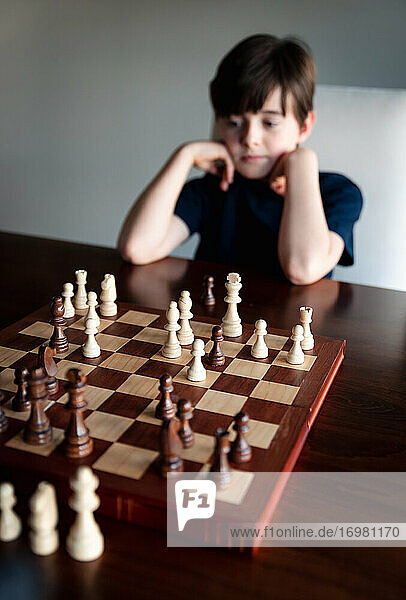 Nachdenklicher Junge sitzt hinter einem Schachbrett und betrachtet die Figuren.