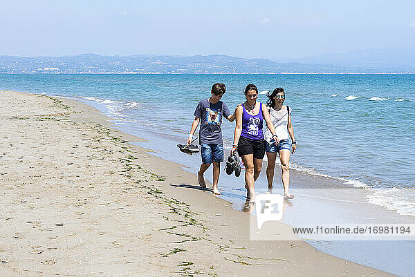 Front view of family walking barefoot on seashore beach on sunny day