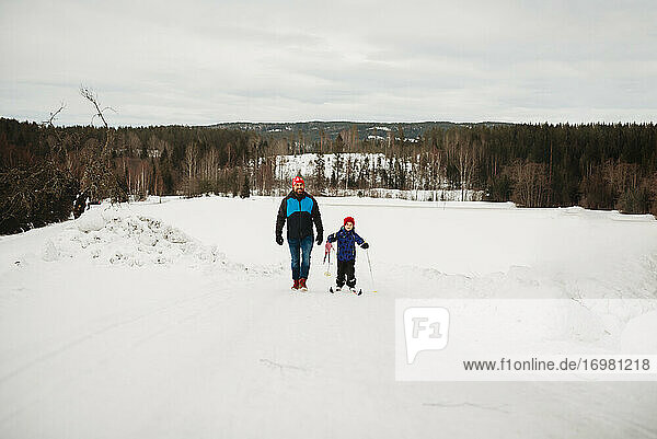 Father and son walking up a slope with skis in snowy winter day Norway