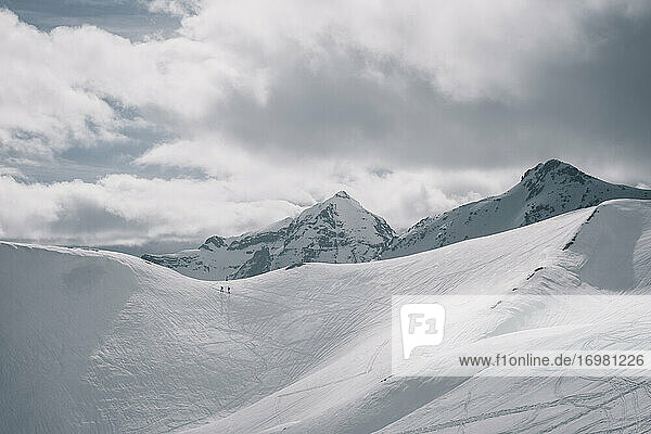 Zwei unerkennbare Skitourengeher am Grat vor einem schneebedeckten Gipfel