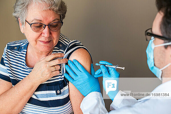 Ältere Frau  der ein Arzt einen Impfstoff in den Oberarm spritzt.