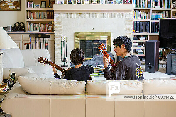 A father and son sit together on couch playing classical guitar music