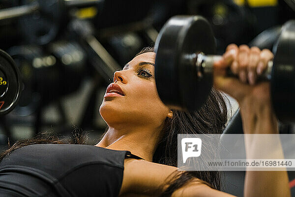 fit woman bench pressing with dumbbells inside a gym