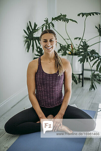 Lächelnder Yogalehrer im Heimstudio  der im Schneidersitz auf einer Yogamatte sitzt