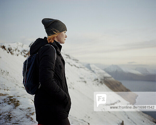 Woman standing on snowy mountain top looking out towards ocean