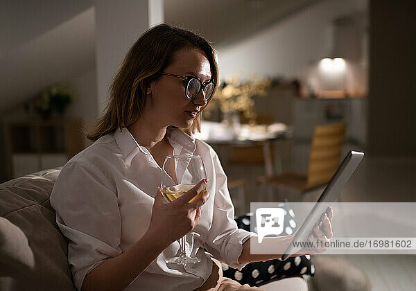 Junge Frau mit einem Glas Wein und einem Tablet zu Hause