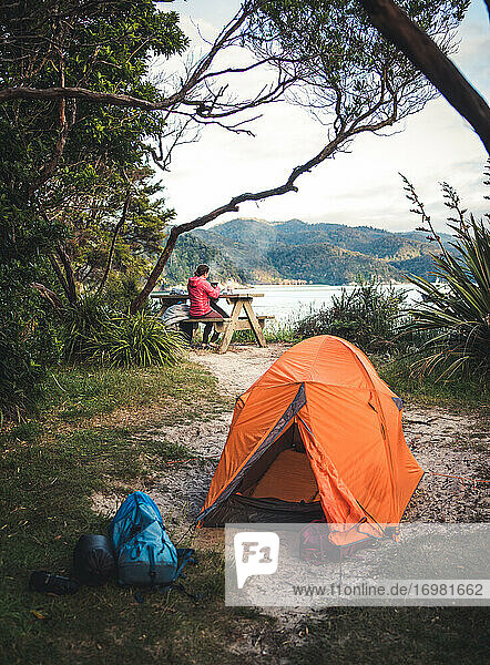 Orangefarbenes Zelt auf einem Campingplatz mit einer Frau  die im Hintergrund Kaffee kocht