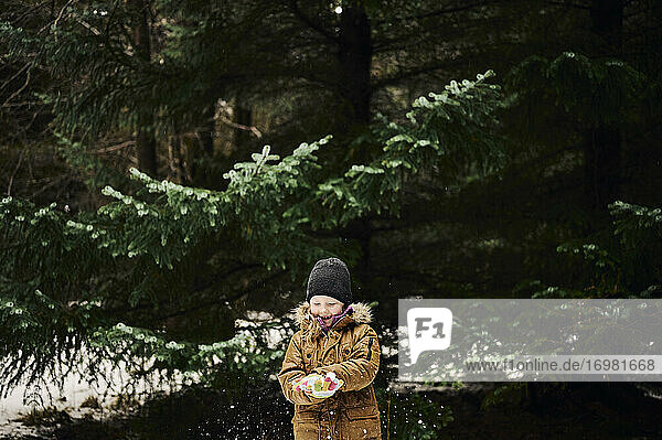 Happy child making snowball near fir tree in forest